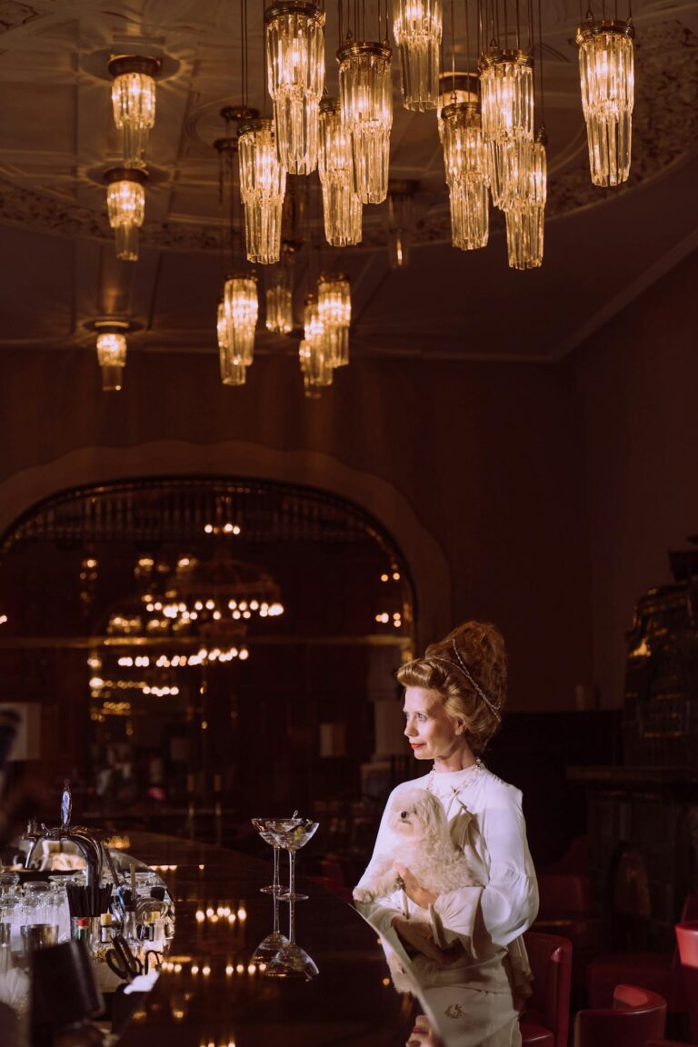 Sophisticated woman with a dog in a lavish, chandelier-lit bar interior.